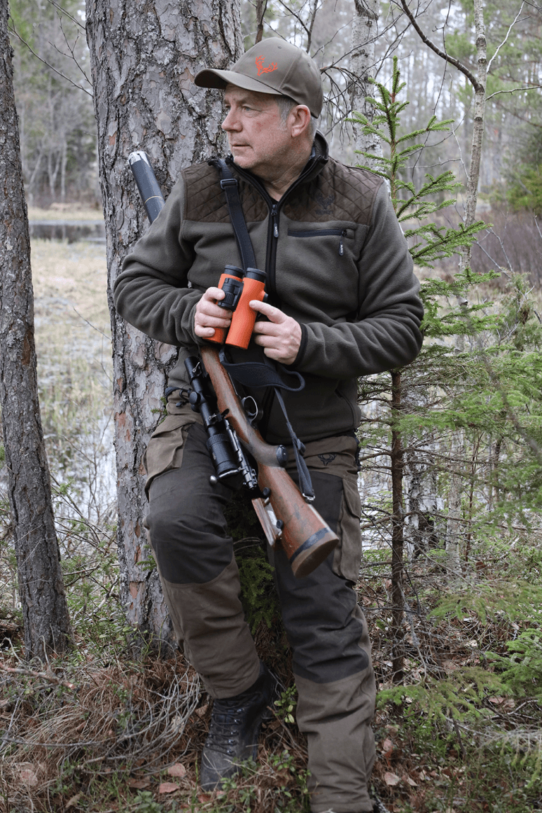 Thomas på jakt i svensk skog, med handkikare och kulgevär över axeln